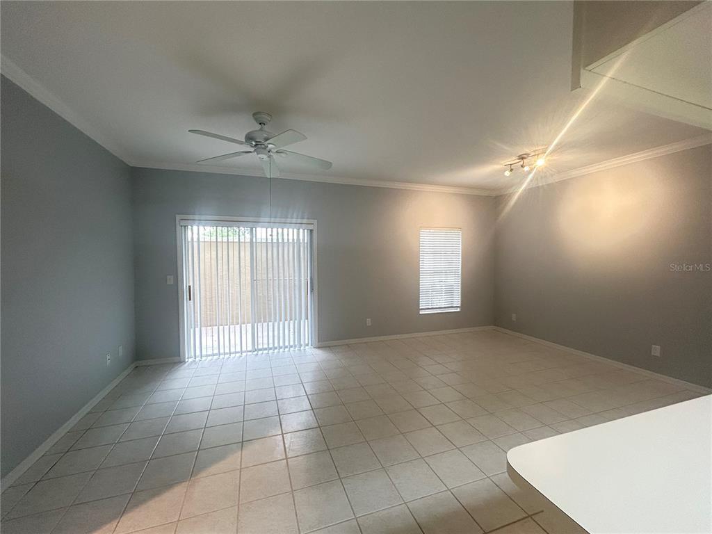 An empty living room features light gray walls, white tile flooring, and a sliding glass door — 1202 EAGLE POND DRIVE UNIT 1202, WINTER HAVEN, FL