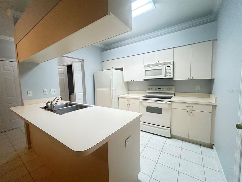 A kitchen features white cabinets, white appliances, a central island with a sink, and tile flooring — 1202 EAGLE POND DRIVE UNIT 1202, WINTER HAVEN, FL