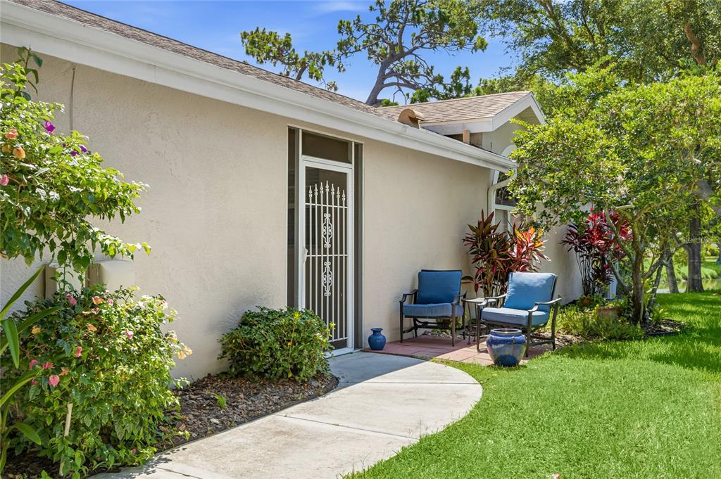 A concrete walkway leads to a white door with a security gate and patio chairs — 7317 ELEANOR CIRCLE UNIT 176, SARASOTA, FL
