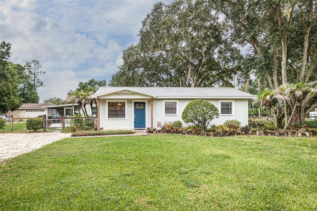 A single-story house with a blue front door, metal roof, and large trees in front — 2220 MINI RANCH ROAD, LAKELAND, FL