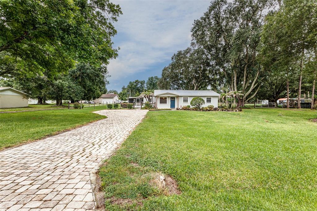 A single-story house with a paved driveway sits on a large, tree-filled grassy lot — 2220 MINI RANCH ROAD, LAKELAND, FL