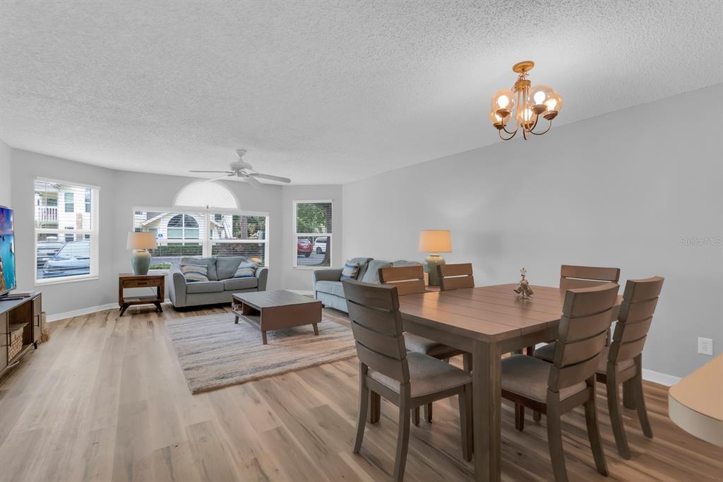 An open-concept living and dining area features light wood flooring, neutral walls, and a chandelier — 5004 LAGUNA BAY CIRCLE UNIT 49, KISSIMMEE, FL