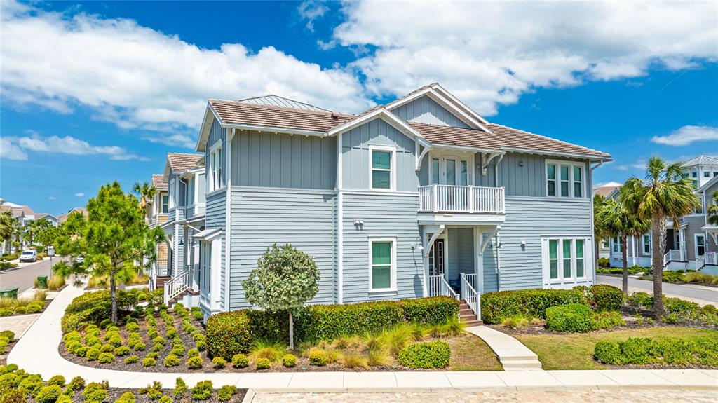 A two-story blue house with white trim and a balcony stands on a landscaped corner — 283 SAINT LUCIA DRIVE UNIT 101, BRADENTON, FL