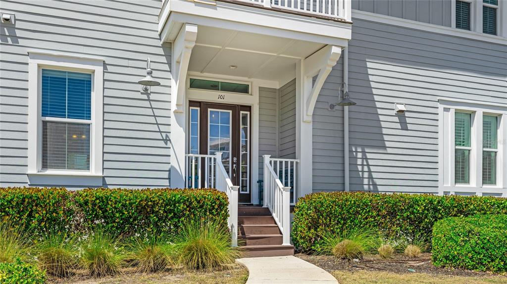 The exterior of a gray house features a covered front porch with stairs and landscaping — 283 SAINT LUCIA DRIVE UNIT 101, BRADENTON, FL