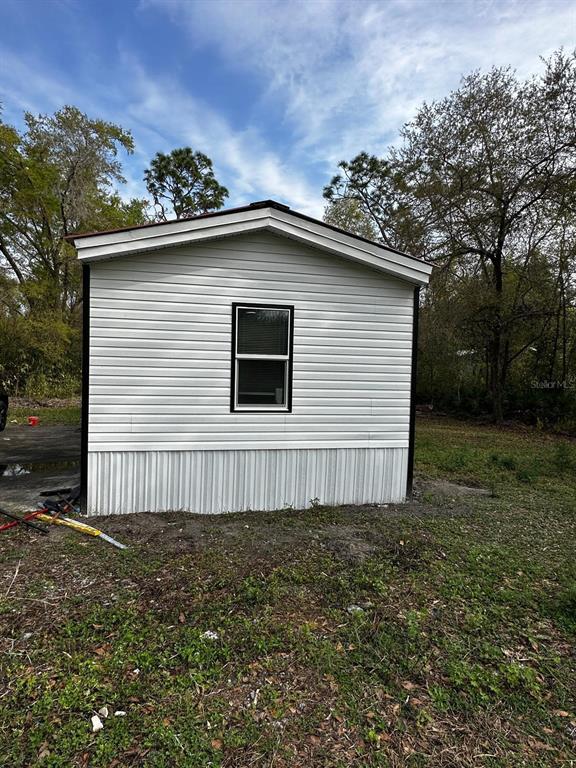The exterior of a small, white-sided mobile home features a single window and metal skirting — 343 CREEKWOOD RUN, LAKELAND, FL