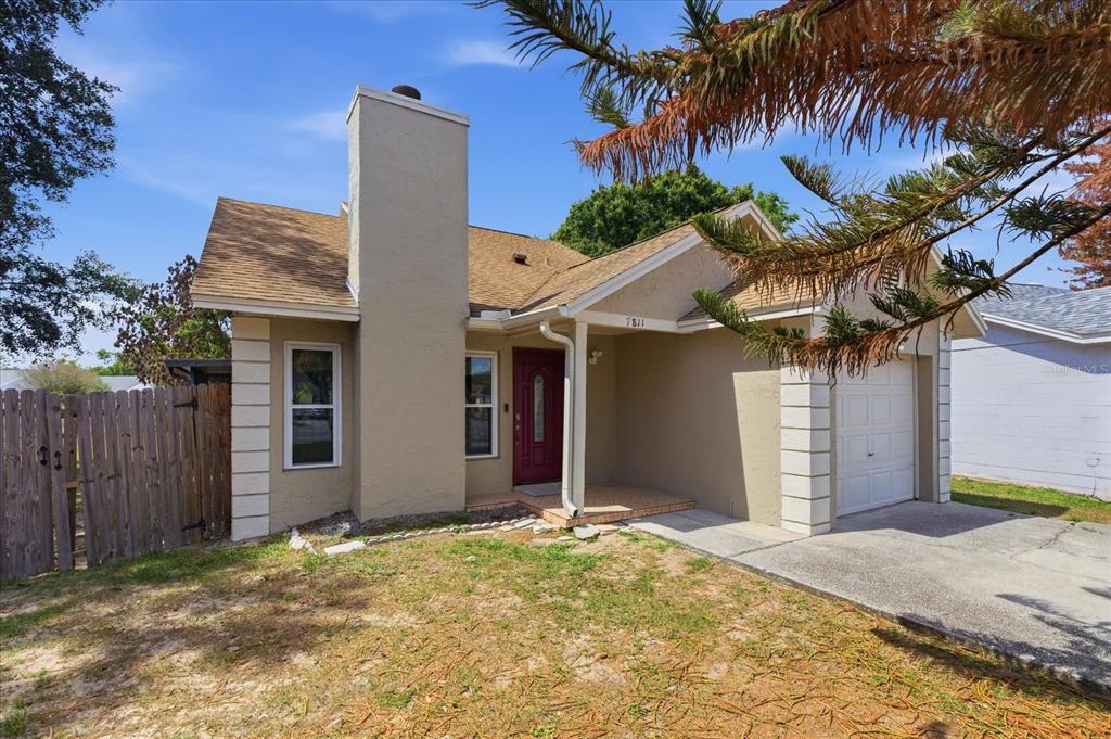 A tan, single-story house with a red front door, a chimney, and a one-car garage — 7811 WORTHAM COURT, ORLANDO, FL