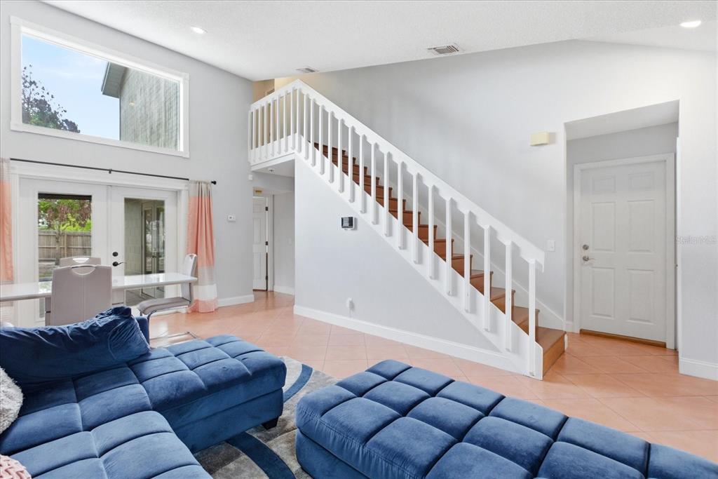 A living room features a blue sectional sofa, tiled floors, and a staircase with white railings — 7811 WORTHAM COURT, ORLANDO, FL