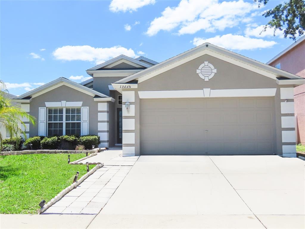 A single-story suburban house features a two-car garage, gray stucco siding, and white trim — 13226 EVENING SUNSET LANE, RIVERVIEW, FL