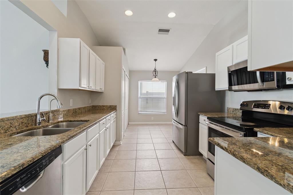 A kitchen features white cabinets, granite countertops, stainless steel appliances, and tile flooring — 13226 EVENING SUNSET LANE, RIVERVIEW, FL