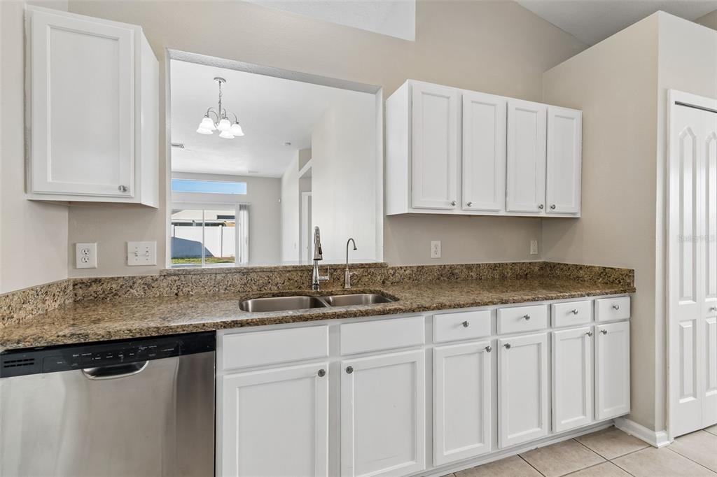 A kitchen features white cabinets, granite countertops, a stainless steel dishwasher, and a pass-through window — 13226 EVENING SUNSET LANE, RIVERVIEW, FL