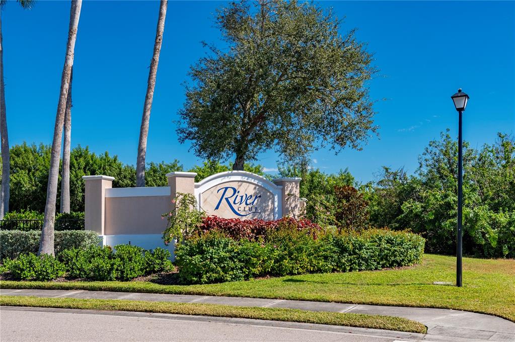 A stone monument sign for River Club stands in a landscaped area with palm trees — 24311 RIVERFRONT DRIVE, PUNTA GORDA, FL