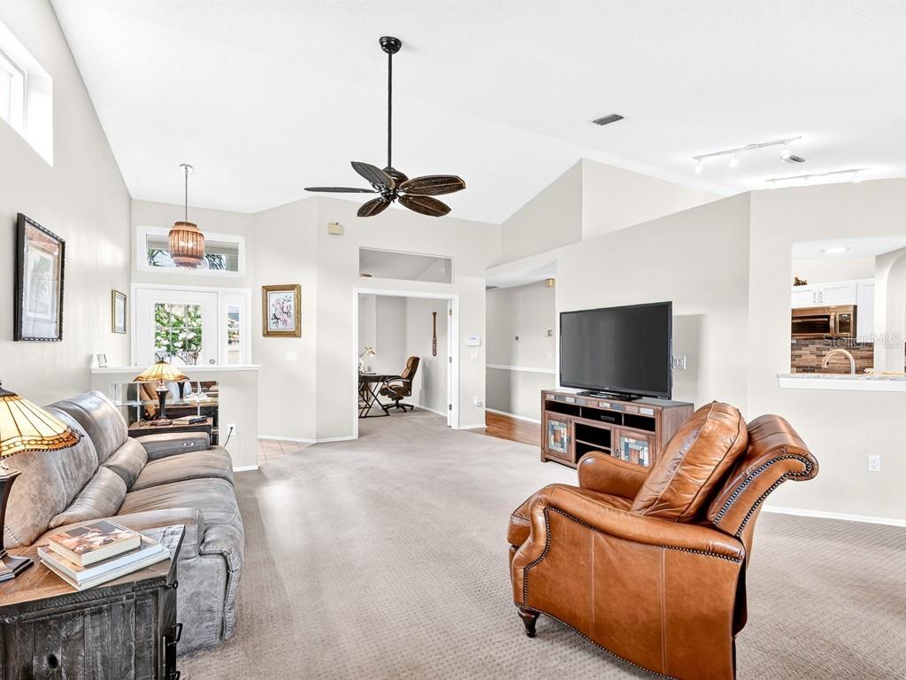 A living room features a vaulted ceiling, a ceiling fan, carpeted floors, and a television — 4322 EDENROSE WAY UNIT 86, SARASOTA, FL