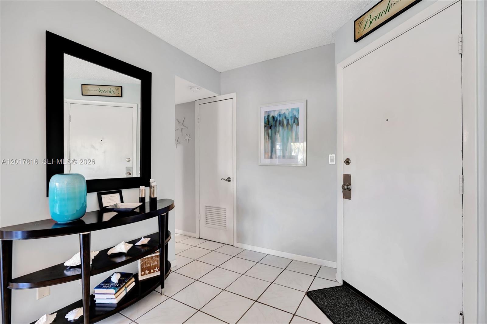 An entryway features white tile floors, a black console table, a mirror, and a white door — 1605 S Us Highway 1, Jupiter FL 33477, JUPITER, FL