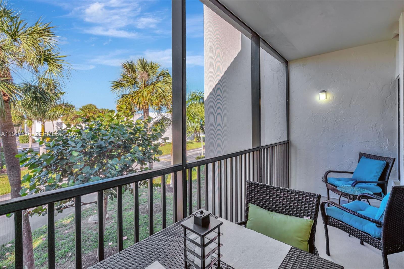 A screened-in balcony features wicker furniture, a small table, and views of palm trees — 1605 S Us Highway 1, Jupiter FL 33477, JUPITER, FL