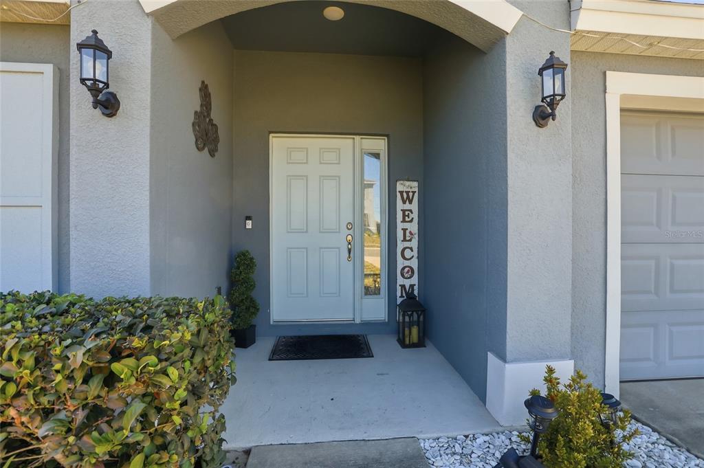The exterior entrance features a white front door, a welcome sign, and two wall lanterns — 3536 YARIAN DRIVE, HAINES CITY, FL