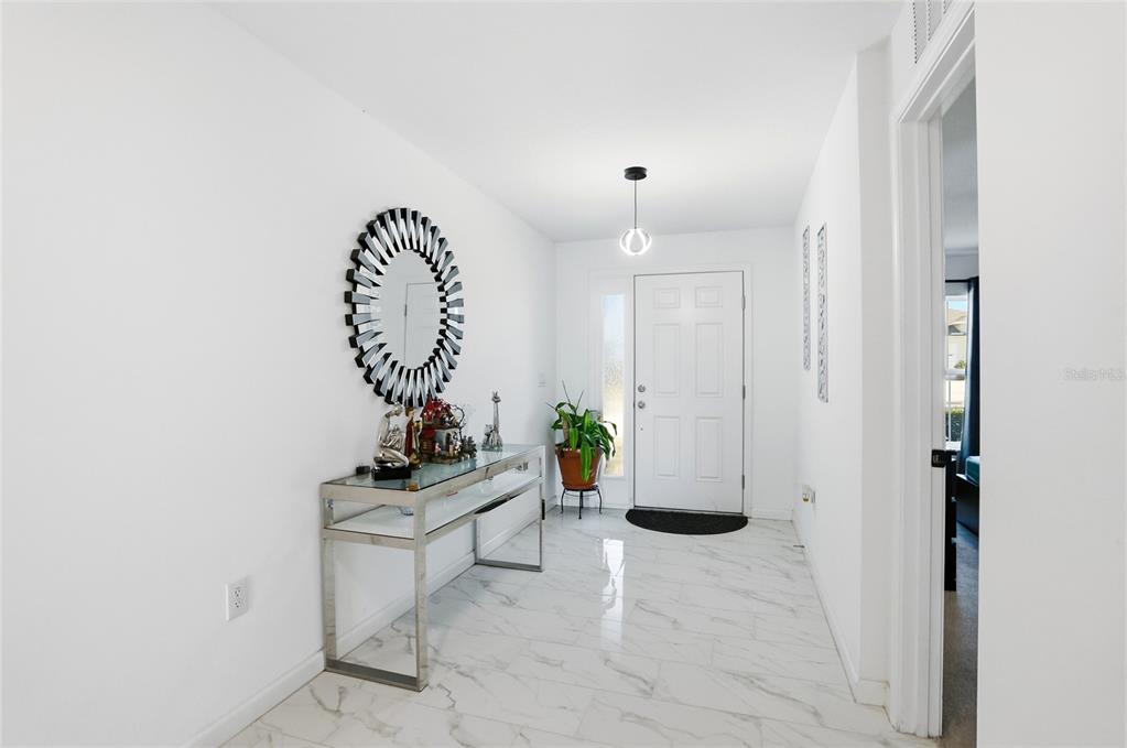 A bright entryway features white marble-look tile flooring, a glass console table, and a mirror — 3536 YARIAN DRIVE, HAINES CITY, FL