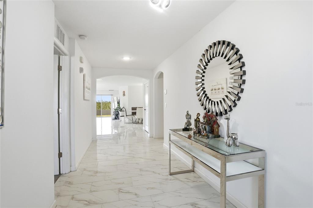 A bright hallway features white marble-look tile flooring, a glass console table, and a sunburst mirror — 3536 YARIAN DRIVE, HAINES CITY, FL