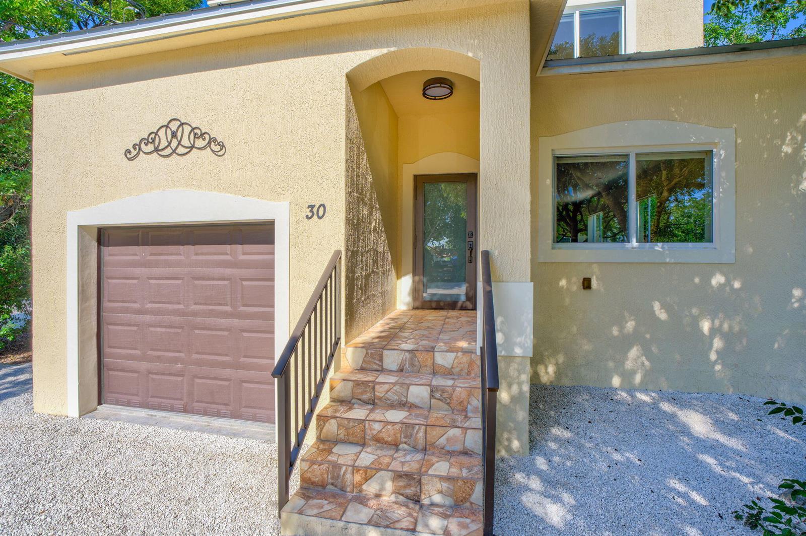 A two-story yellow house with a brown garage door sits behind a gravel driveway — 30 Seagate Boulevard, Key Largo FL 33037, KEY LARGO, FL