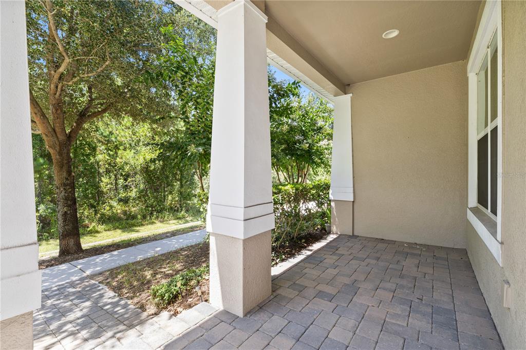 A covered front porch features a paver floor, white columns, and a view of trees — 10509 SPRING ARBOR LANE, WINTER GARDEN, FL