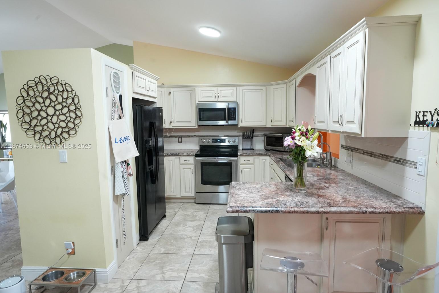 A kitchen features off-white cabinets, stainless steel appliances, and a granite-look countertop — 2304 SE 8TH TER, Cape Coral FL 33990, CAPE CORAL, FL