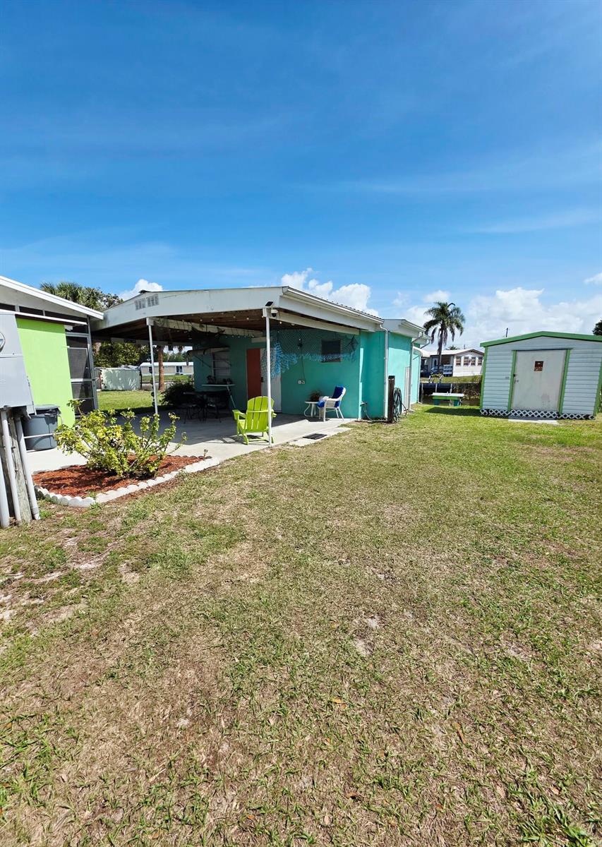 A turquoise house features a covered patio, a small shed, and a grassy backyard — 1501 Lake Drive W, Okeechobee FL 34974, OKEECHOBEE, FL