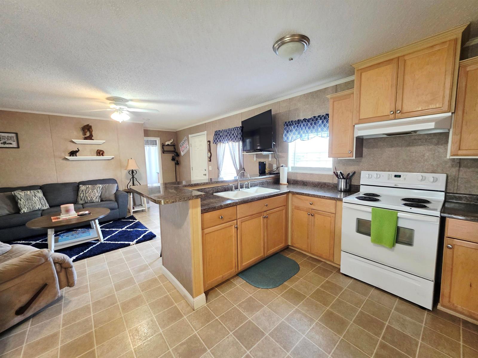 A kitchen with light wood cabinets and a white stove opens into a living area — 1501 Lake Drive W, Okeechobee FL 34974, OKEECHOBEE, FL