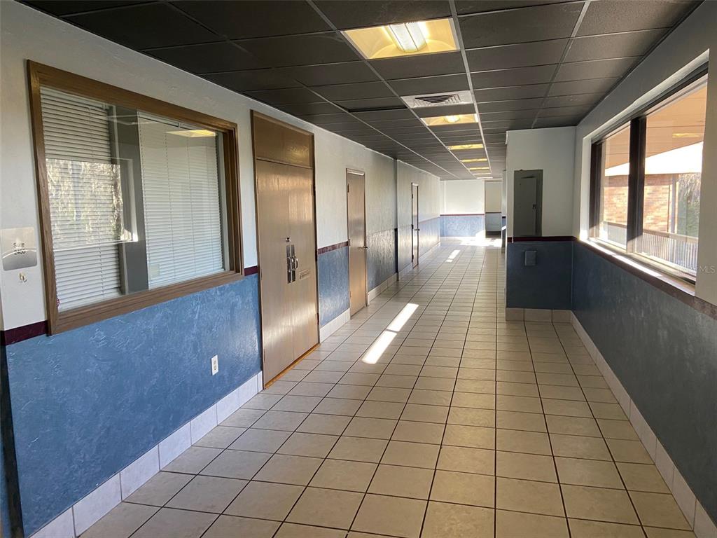 A long, tiled office hallway features blue wainscoting, a dark drop ceiling, and multiple doors — 3501 SW 2ND AVENUE UNIT 2400, GAINESVILLE, FL