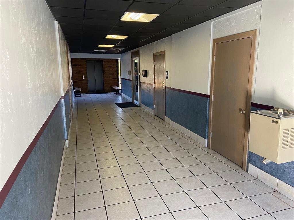 A tiled hallway features a black drop ceiling, blue wainscoting, and a water fountain — 3501 SW 2ND AVENUE UNIT 2400, GAINESVILLE, FL