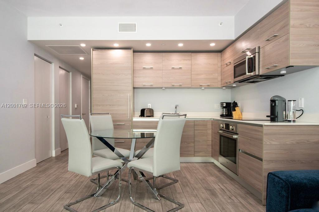 A modern kitchen features light wood cabinetry, a glass dining table, and stainless steel appliances — 1300 S Miami ave. # 3908, Miami FL 33130, MIAMI, FL