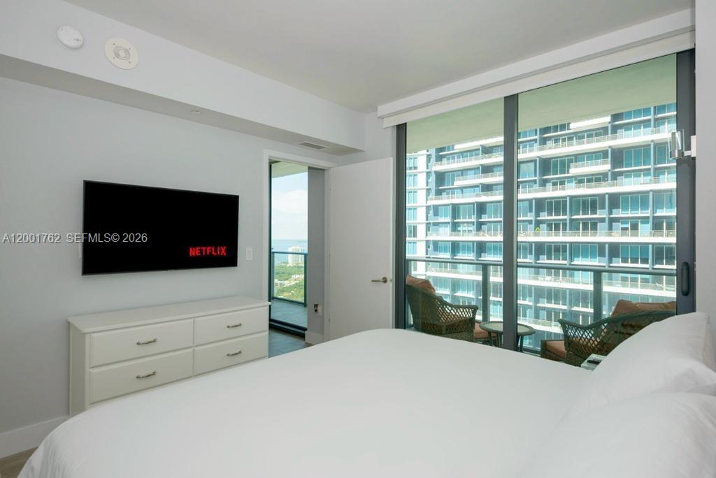 A bedroom features a white dresser, a wall-mounted television, and a balcony overlooking buildings — 1300 S Miami ave. # 3908, Miami FL 33130, MIAMI, FL