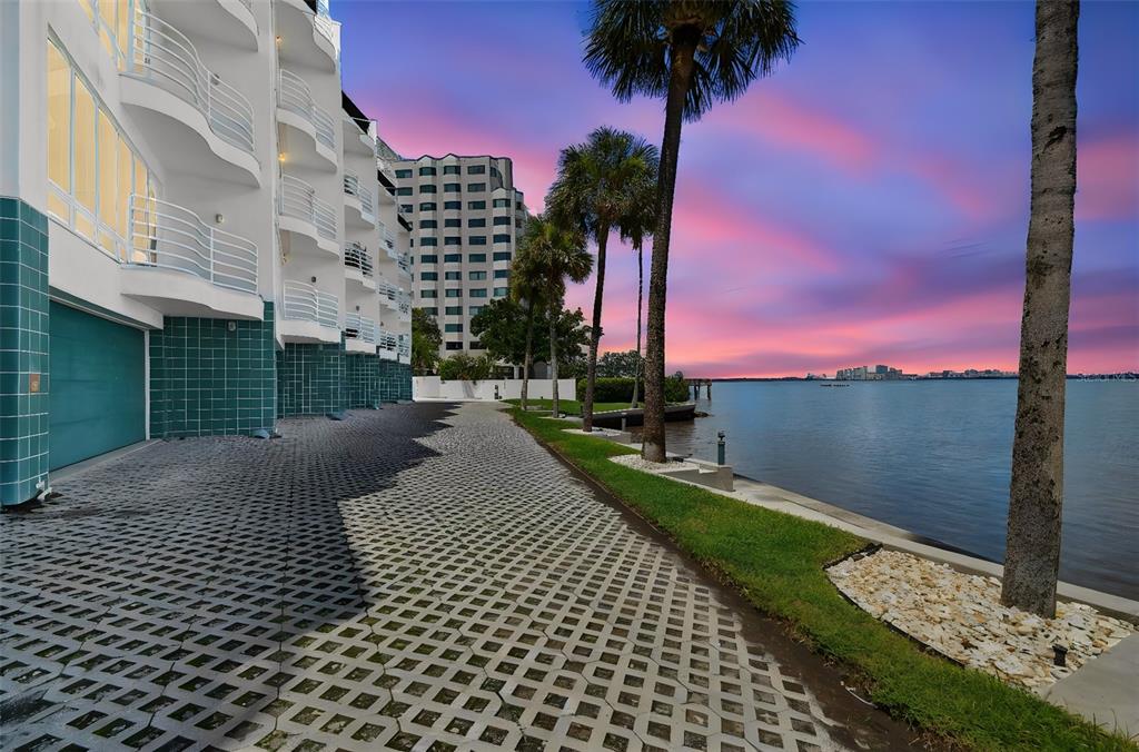 A waterfront view of a multi-story building with balconies and a paved walkway at sunset — 4950 BAYSHORE BOULEVARD UNIT 30, TAMPA, FL