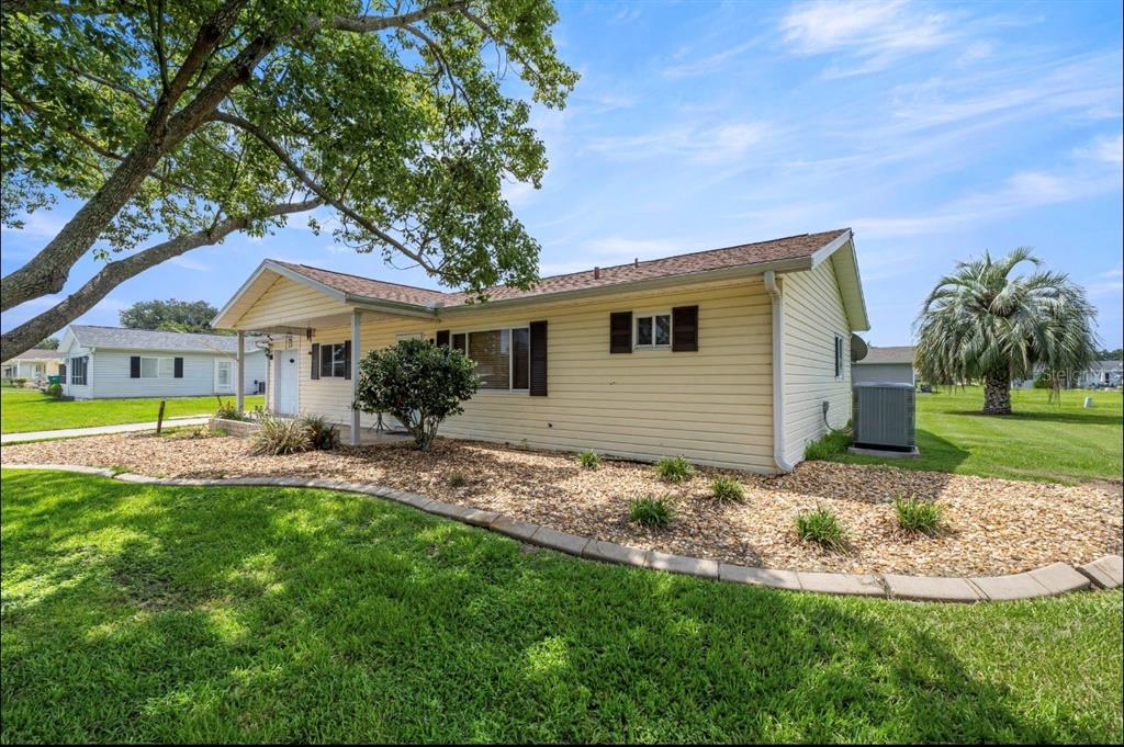 A single-story house with light yellow siding, a covered porch, and a landscaped rock garden — 10358 SE 178 PLACE, SUMMERFIELD, FL