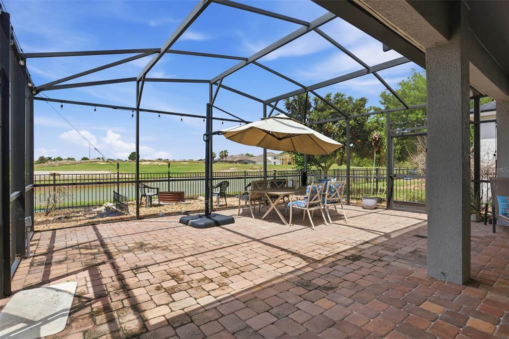 A screened-in patio with paver flooring overlooks a golf course and a small pond — 1409 BROOKHAVEN COURT, DAVENPORT, FL
