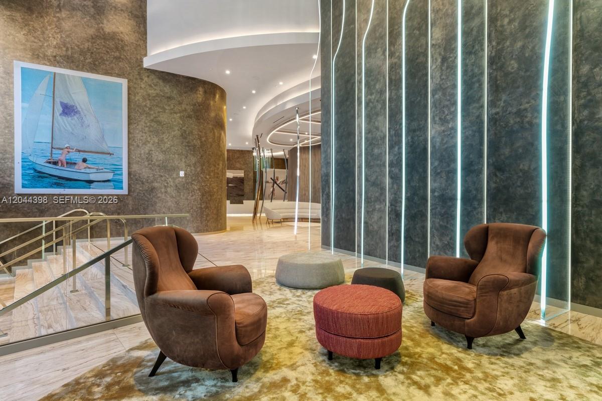A modern lobby features two brown armchairs, circular ottomans, and a large sailboat painting — 1000 Brickell Plz # 3410, Miami FL 33131, MIAMI, FL