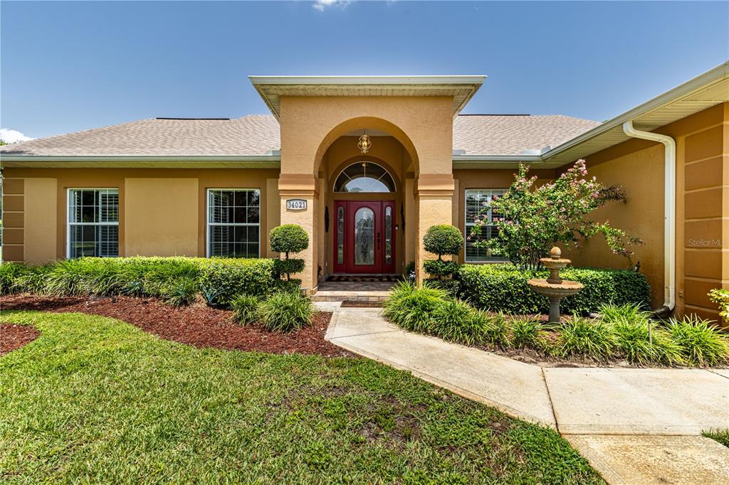 A single-story house with a tan stucco exterior, a red front door, and a lawn — 34021 PARK LANE, LEESBURG, FL