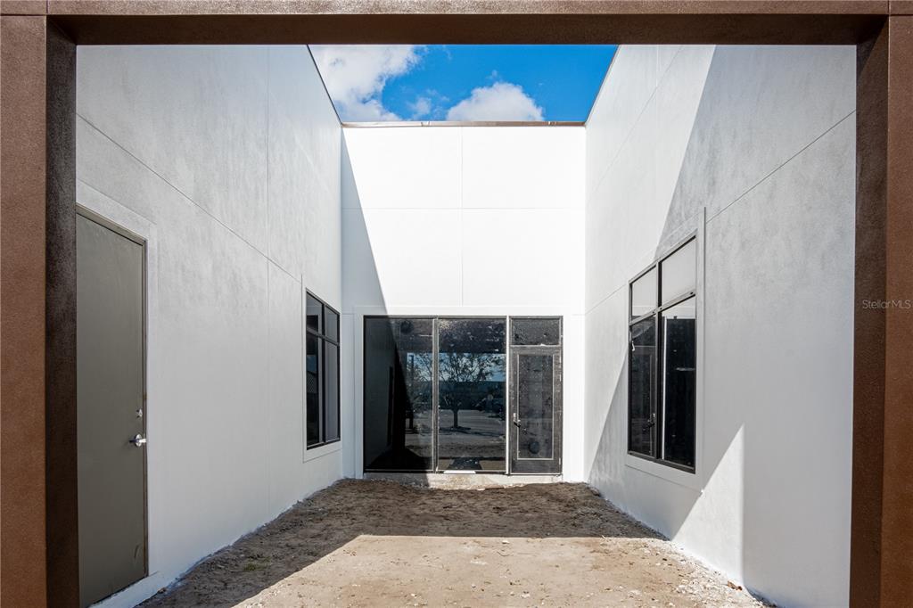 An outdoor courtyard features white walls, dark-framed windows, a door, and a dirt ground surface — 11125 CORRIDOR PLACE, BRADENTON, FL