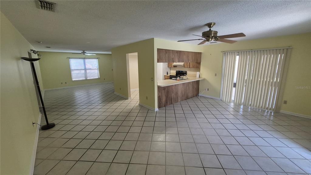 An open-concept living area features light-colored tile flooring, a kitchen with wood cabinets, and sliding doors — 4625 CANTERBURY DRIVE, LAND O LAKES, FL