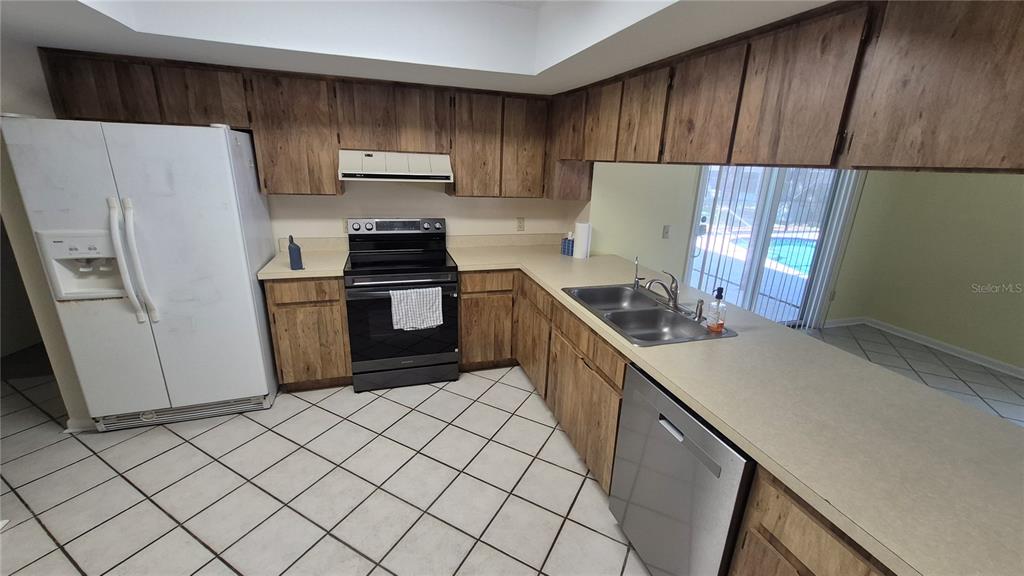 A kitchen features wood cabinets, laminate countertops, tile flooring, and stainless steel appliances — 4625 CANTERBURY DRIVE, LAND O LAKES, FL