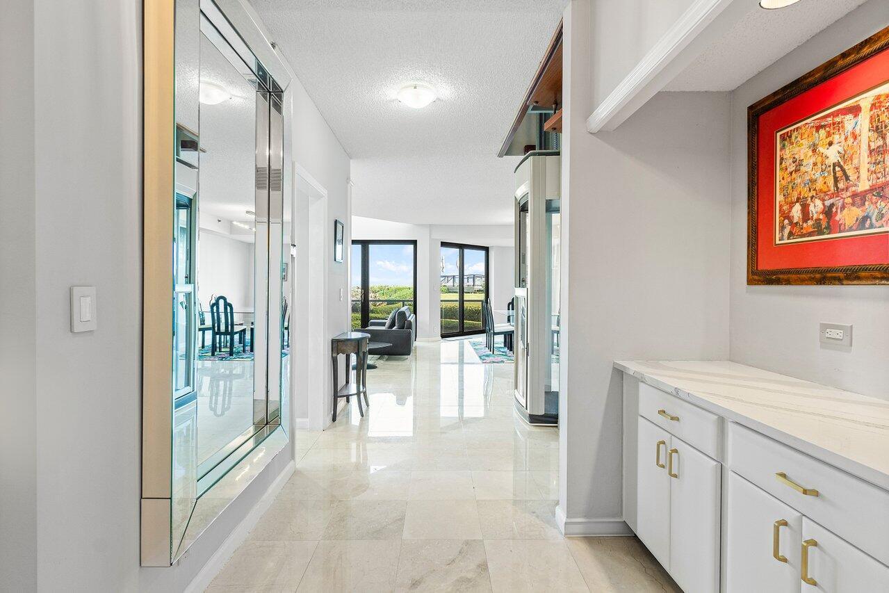 A bright hallway with white tile floors leads to a living area with balcony views — 3120 S Ocean Boulevard # 101, Palm Beach FL 33480, PALM BEACH, FL