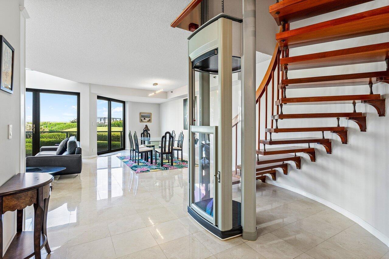 A living and dining area features a glass elevator, wooden staircase, and tile flooring — 3120 S Ocean Boulevard # 101, Palm Beach FL 33480, PALM BEACH, FL