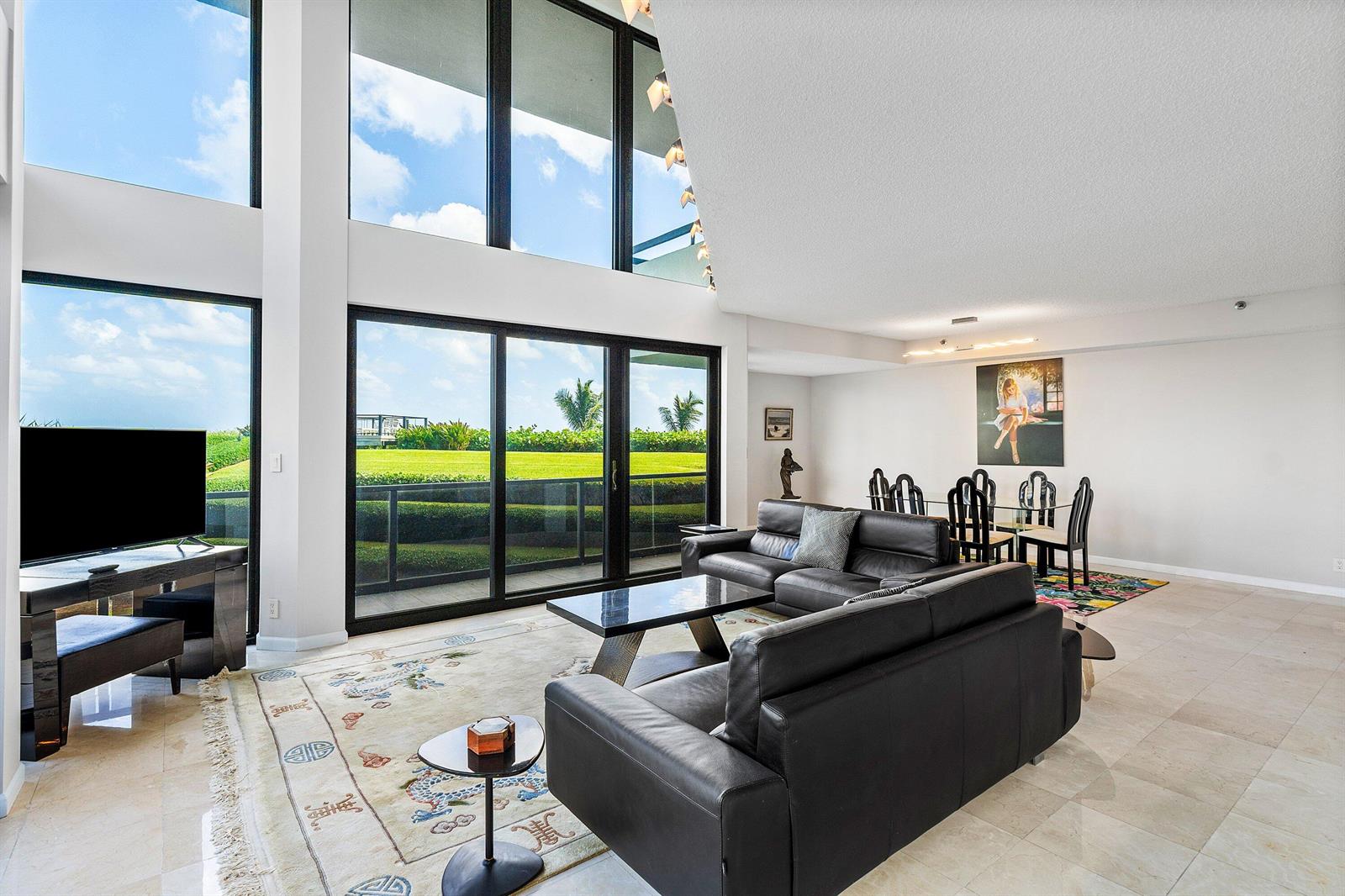 A spacious living and dining area features floor-to-ceiling windows, black leather furniture, and tile flooring — 3120 S Ocean Boulevard # 101, Palm Beach FL 33480, PALM BEACH, FL