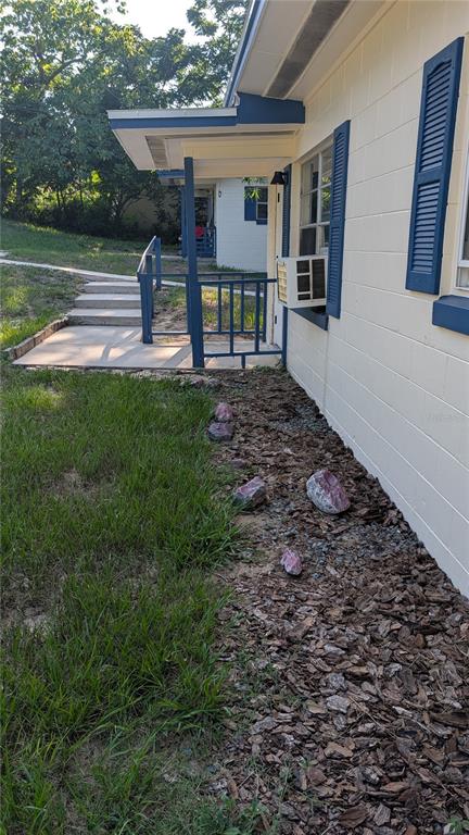 A side view of a house with a covered porch, blue shutters, and wood mulch — 738 E MINNEOLA AVENUE, CLERMONT, FL