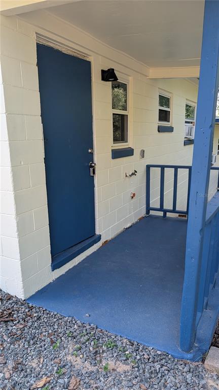 A blue door opens onto a painted porch with a railing against a concrete block wall — 738 E MINNEOLA AVENUE, CLERMONT, FL