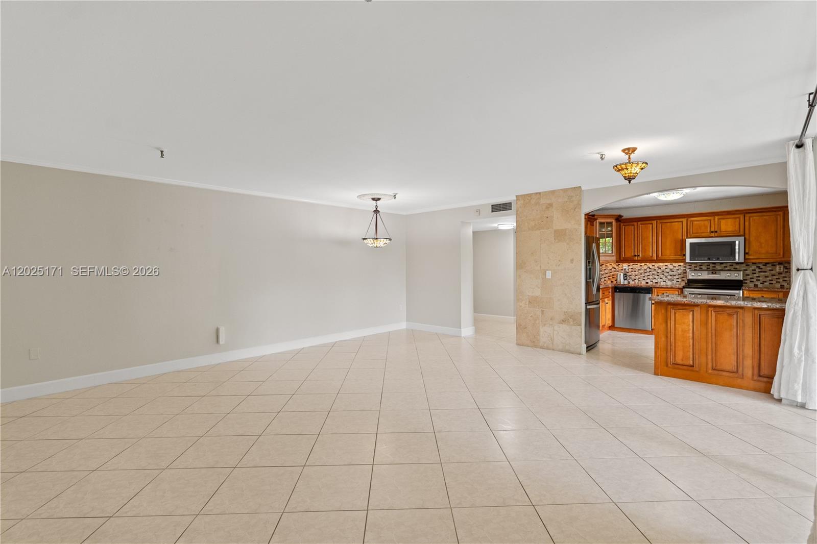 An open living area features tile flooring, a dining light fixture, and a wood kitchen — 671 NE 195th St # 121E, Miami FL 33179, MIAMI, FL