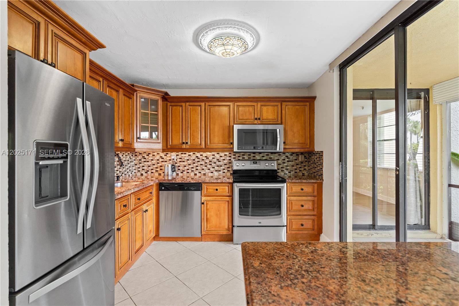 A kitchen features wood cabinets, stainless steel appliances, granite countertops, and a mosaic tile backsplash — 671 NE 195th St # 121E, Miami FL 33179, MIAMI, FL