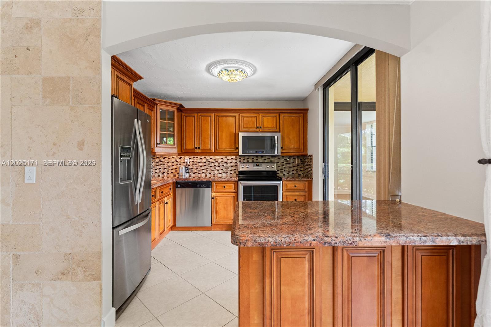 A kitchen features wooden cabinets, granite countertops, stainless steel appliances, and a tiled floor — 671 NE 195th St # 121E, Miami FL 33179, MIAMI, FL