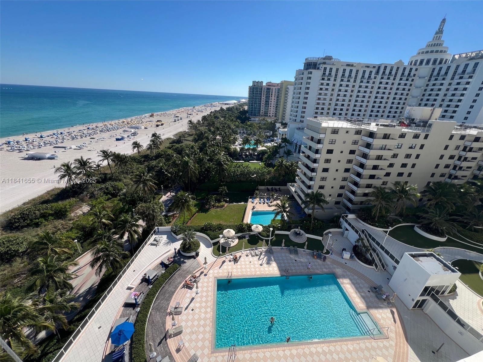 An elevated view of a swimming pool deck, lush landscaping, and a beach with oceanfront buildings — 100 Lincoln Rd # 1419, Miami Beach FL 33139, MIAMI BEACH, FL