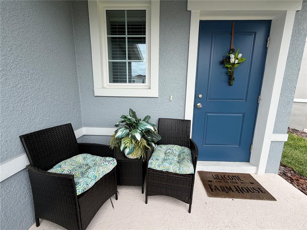 A blue front door and two wicker chairs with patterned cushions sit on a porch — 3030 RUBY FALLS DRIVE, DELAND, FL