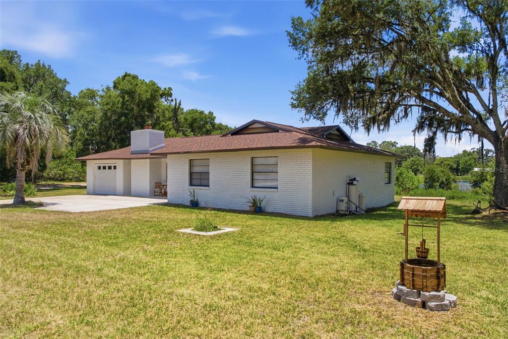A white brick house with a brown roof sits on a grassy lot with a well — 18208 STATE ROAD 52, LAND O LAKES, FL