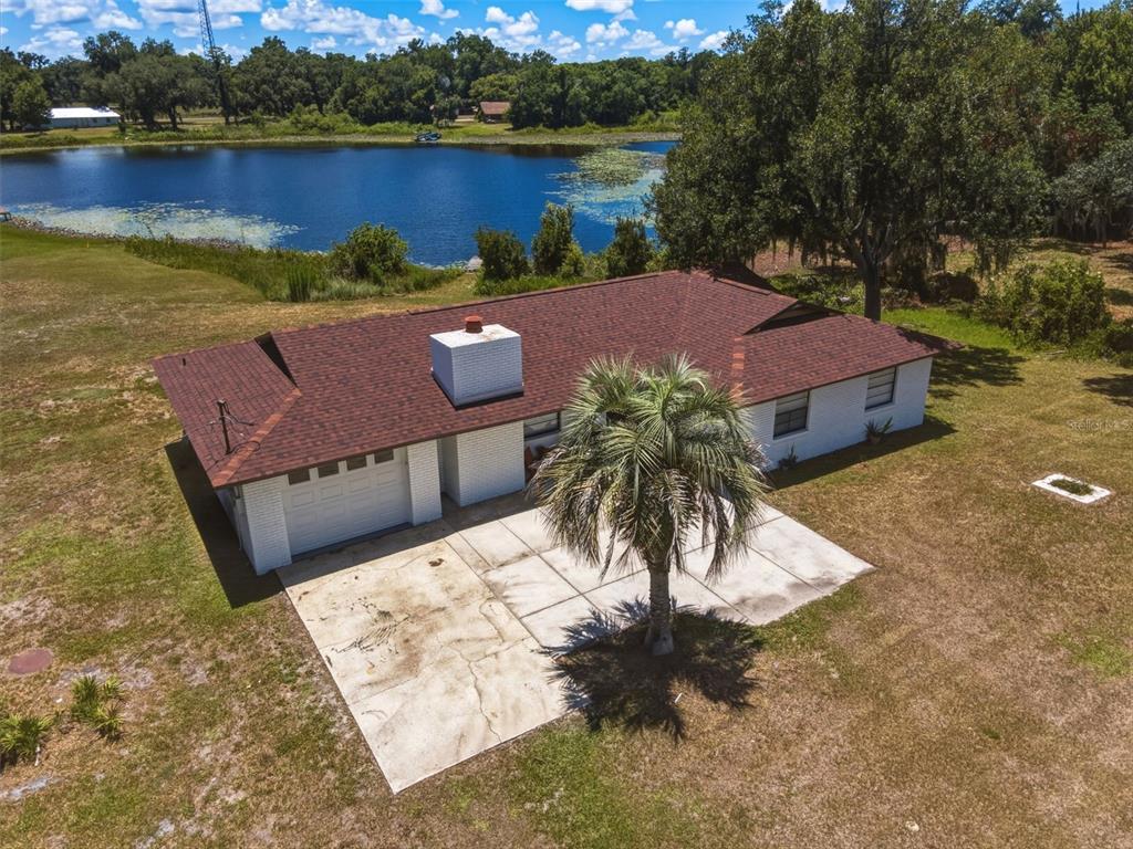 An aerial view shows a white brick house with a brown roof near a lake — 18208 STATE ROAD 52, LAND O LAKES, FL